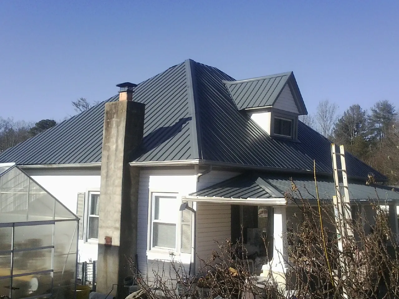 Dark blue standing seam metal roof on a white farmhouse with dormer — Slate & Tile Roof Repair by Roofing Brothers in New Sharon