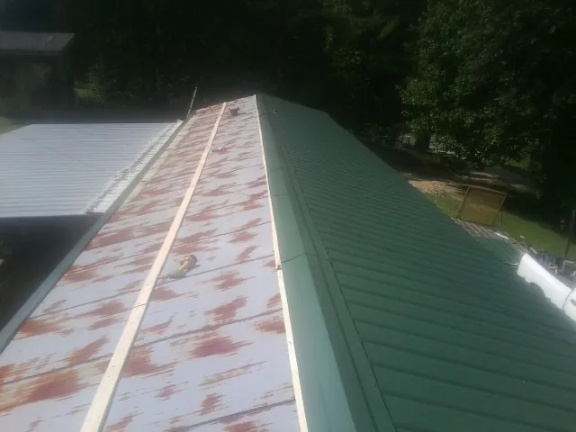 Old rusted panels beside newly installed green metal roofing — Wind Damage Roof Repair by Roofing Brothers in New Sharon