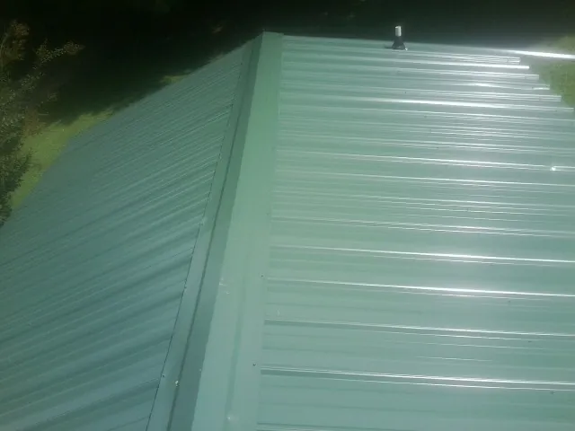 New green metal panels meeting at the ridge of a roof — Flat Roof Repair work by our crew in New Sharon