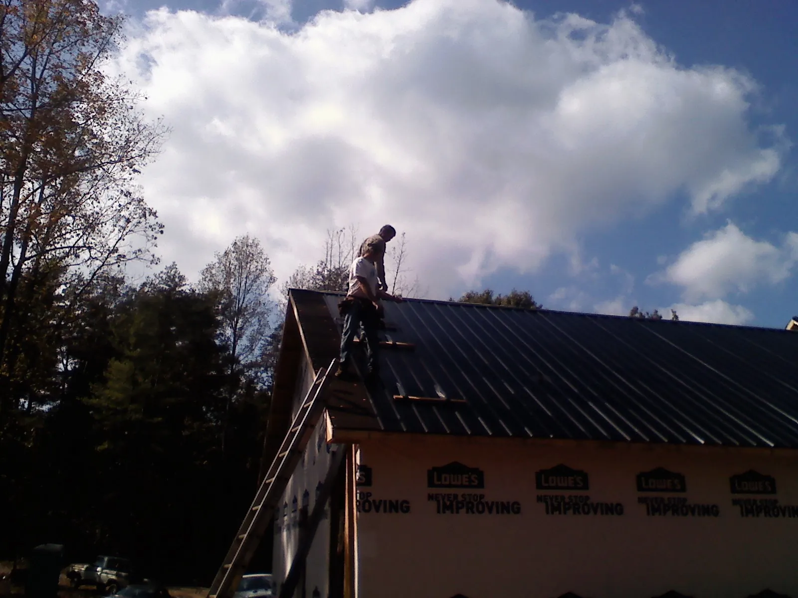 Roofer fastening dark metal panels high against a cloudy sky, from a Roof Inspection job in New Sharon