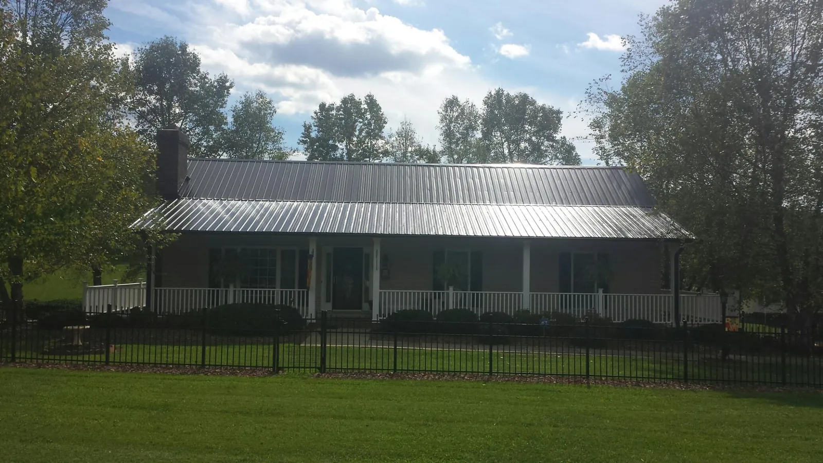 Gray metal roof on a brick ranch with a full width front porch — Gutter Guard Installation work by our crew in New Sharon