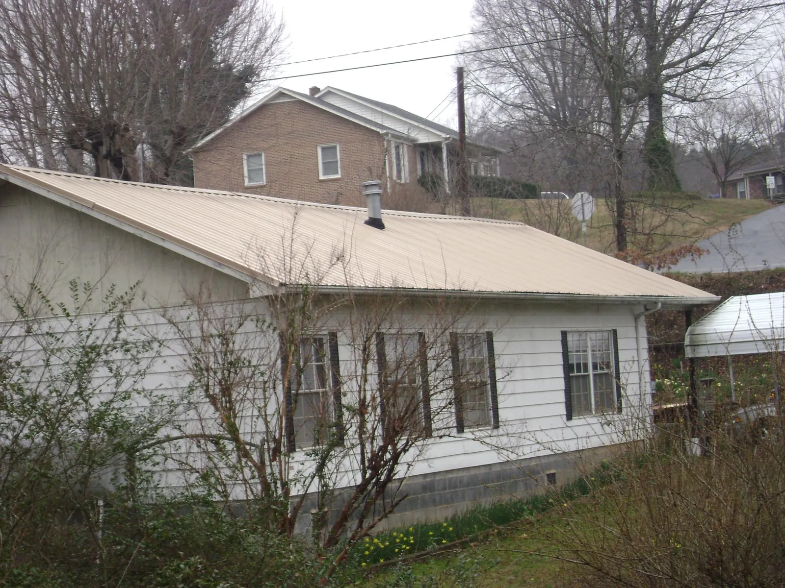 Tan metal roof on a white sided house set into a hillside — Commercial Roofing by Roofing Brothers in New Sharon