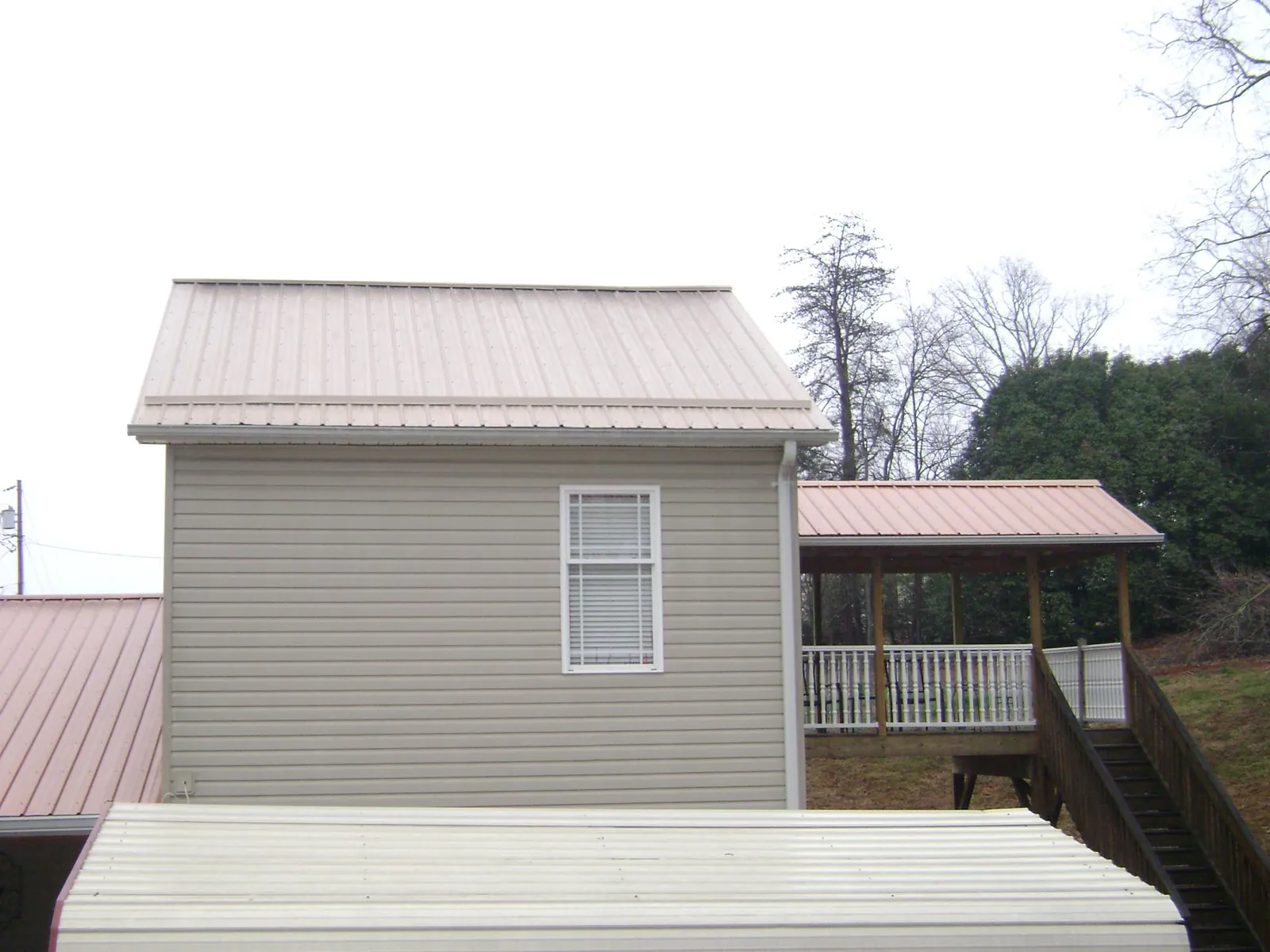 Tan metal roofs on a two story addition and attached porch, from a Roof Replacement job in New Sharon